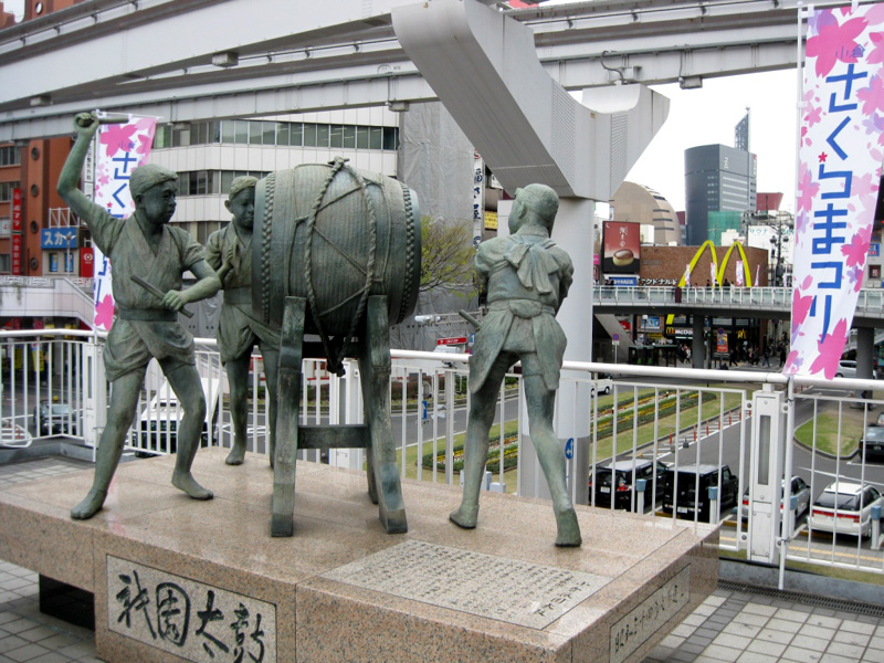 JR小倉駅前にある小倉祇園太鼓の銅像。右奥に会場の1つとなったリバーウォーク北九州が見える