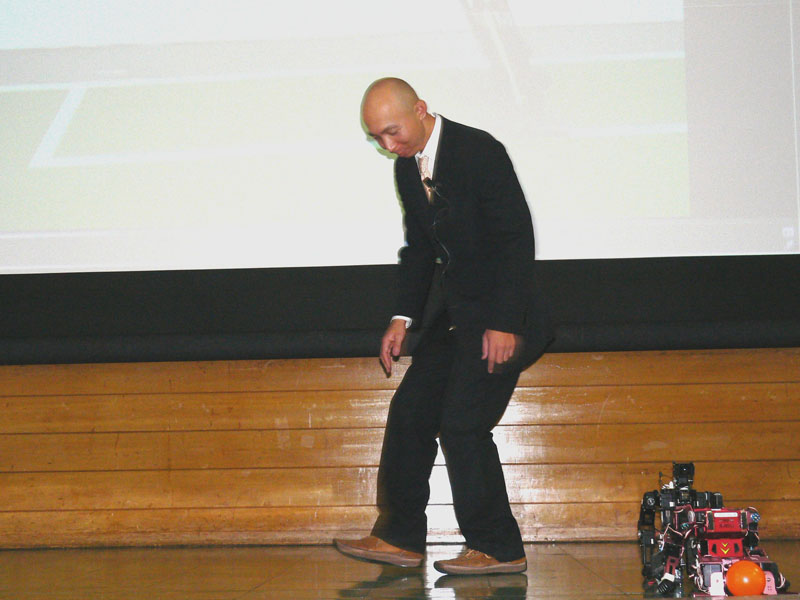 膝を曲げたロボットの歩行を真似る坂本氏